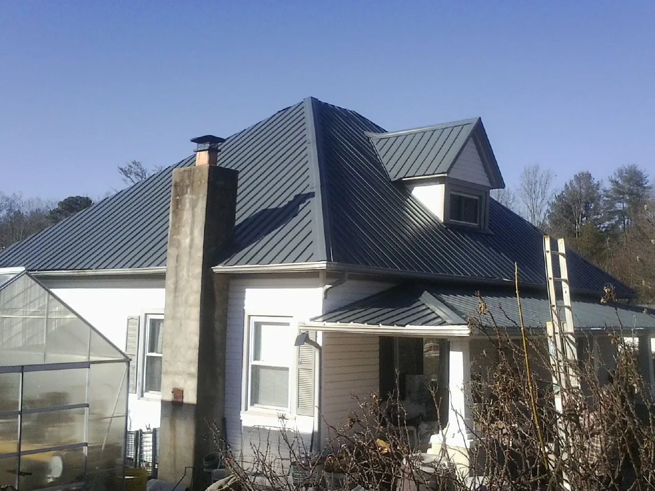 Dark blue standing seam metal roof on a white farmhouse with dormer — Slate & Tile Roof Repair by Roofing Brothers in Heron