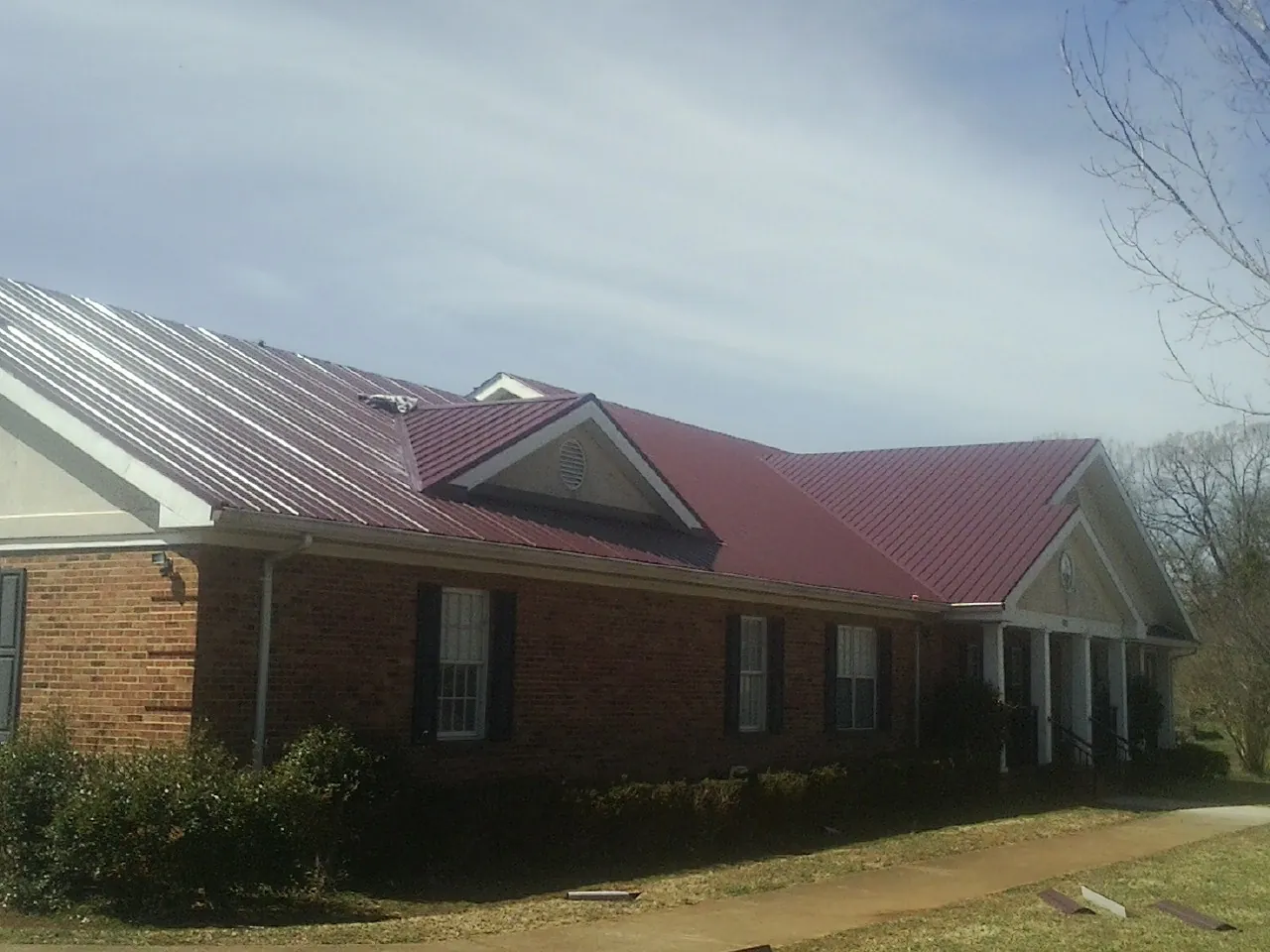 Red metal roof with gabled entries on a long brick building, from a Hail Damage Roof Repair job in Heron