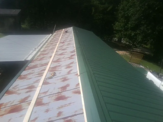 Old rusted panels beside newly installed green metal roofing — Wind Damage Roof Repair by Roofing Brothers in Heron