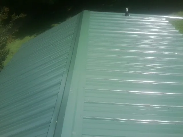 New green metal panels meeting at the ridge of a roof — Flat Roof Repair work by our crew in Heron