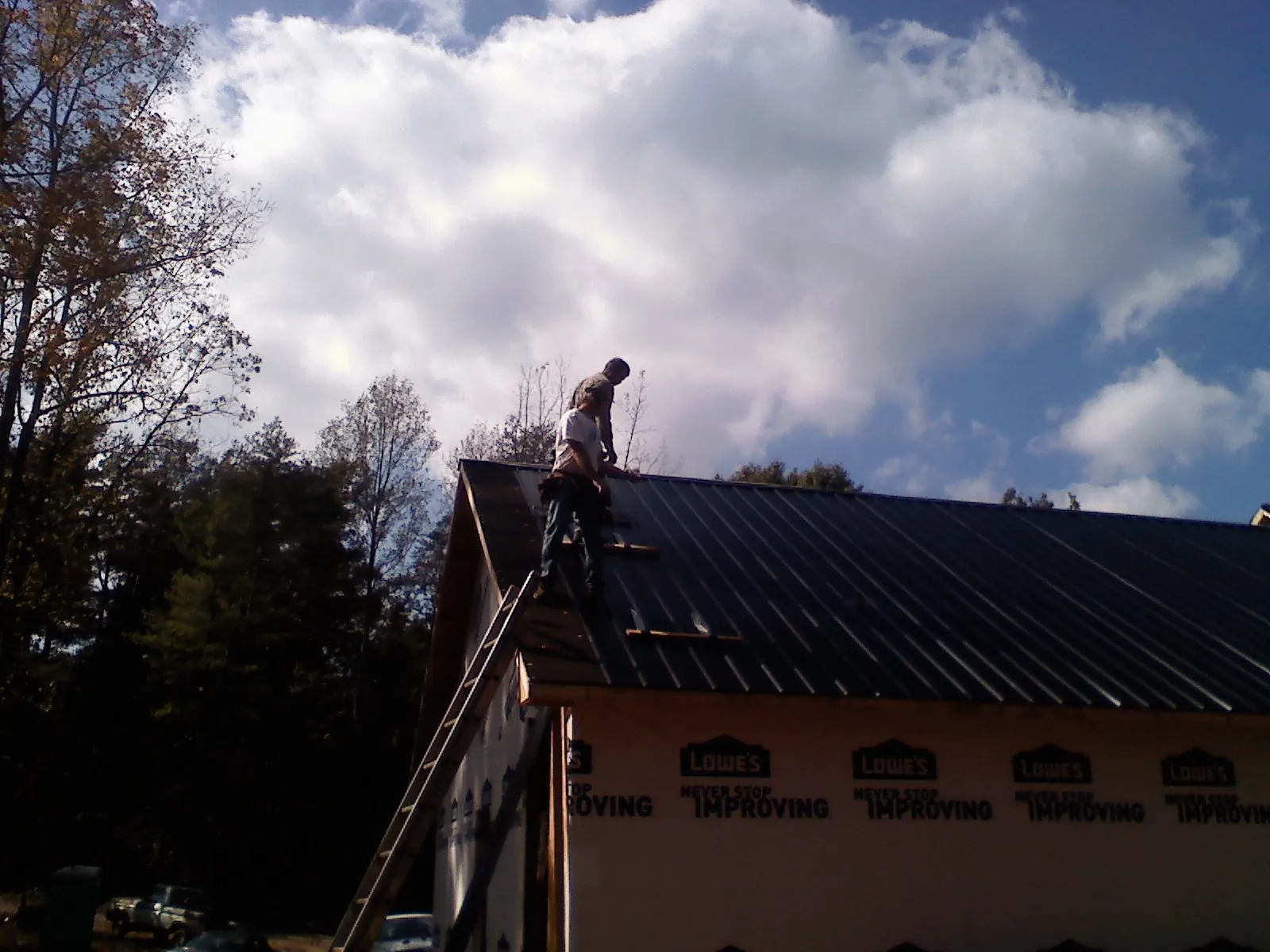 Roofer fastening dark metal panels high against a cloudy sky, from a Roof Inspection job in Heron