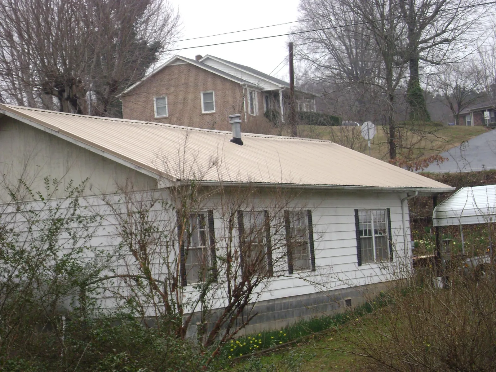 Tan metal roof on a white sided house set into a hillside — Commercial Roofing by Roofing Brothers in Heron