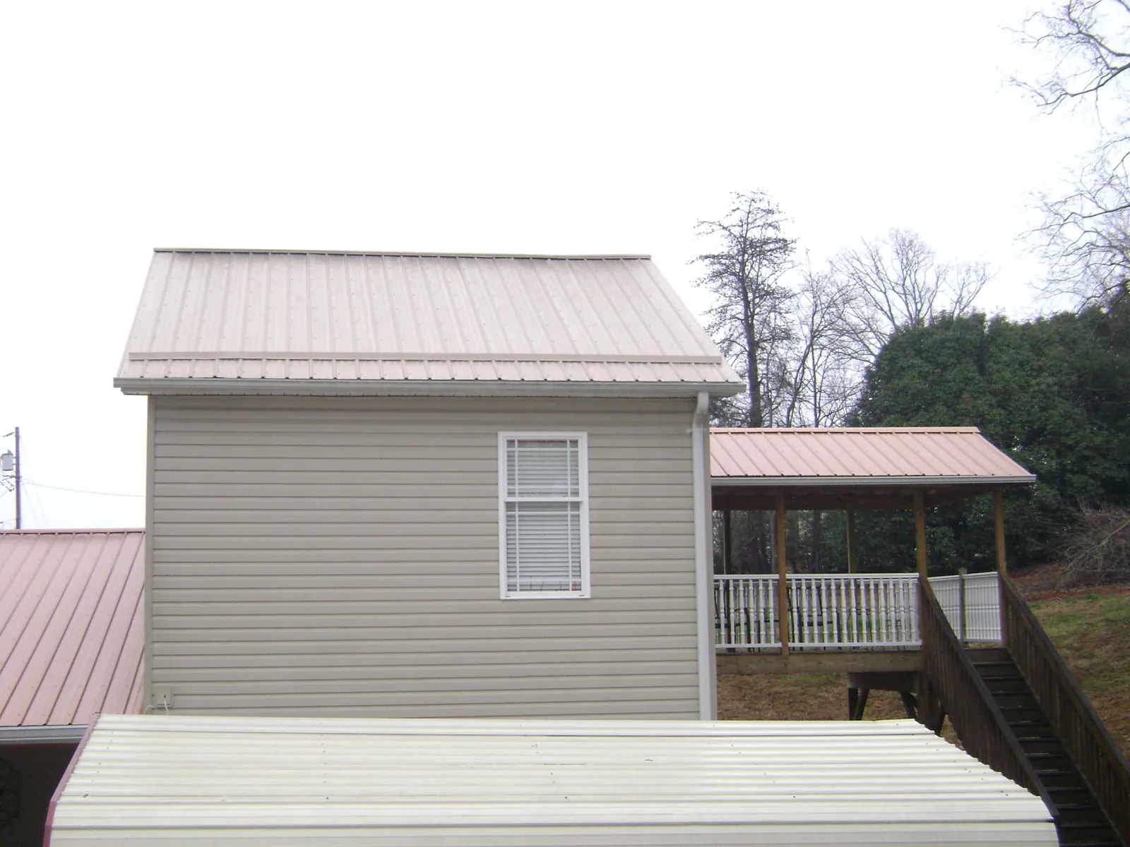 Tan metal roofs on a two story addition and attached porch, from a Roof Replacement job in Heron